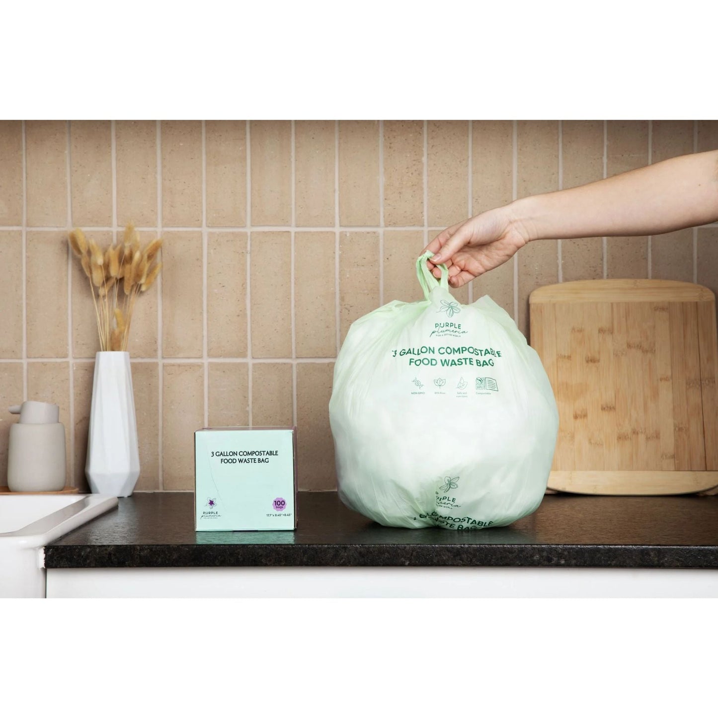 Person holding a 3 gallon compostable food waste bag on a kitchen counter with a tiled wall background.