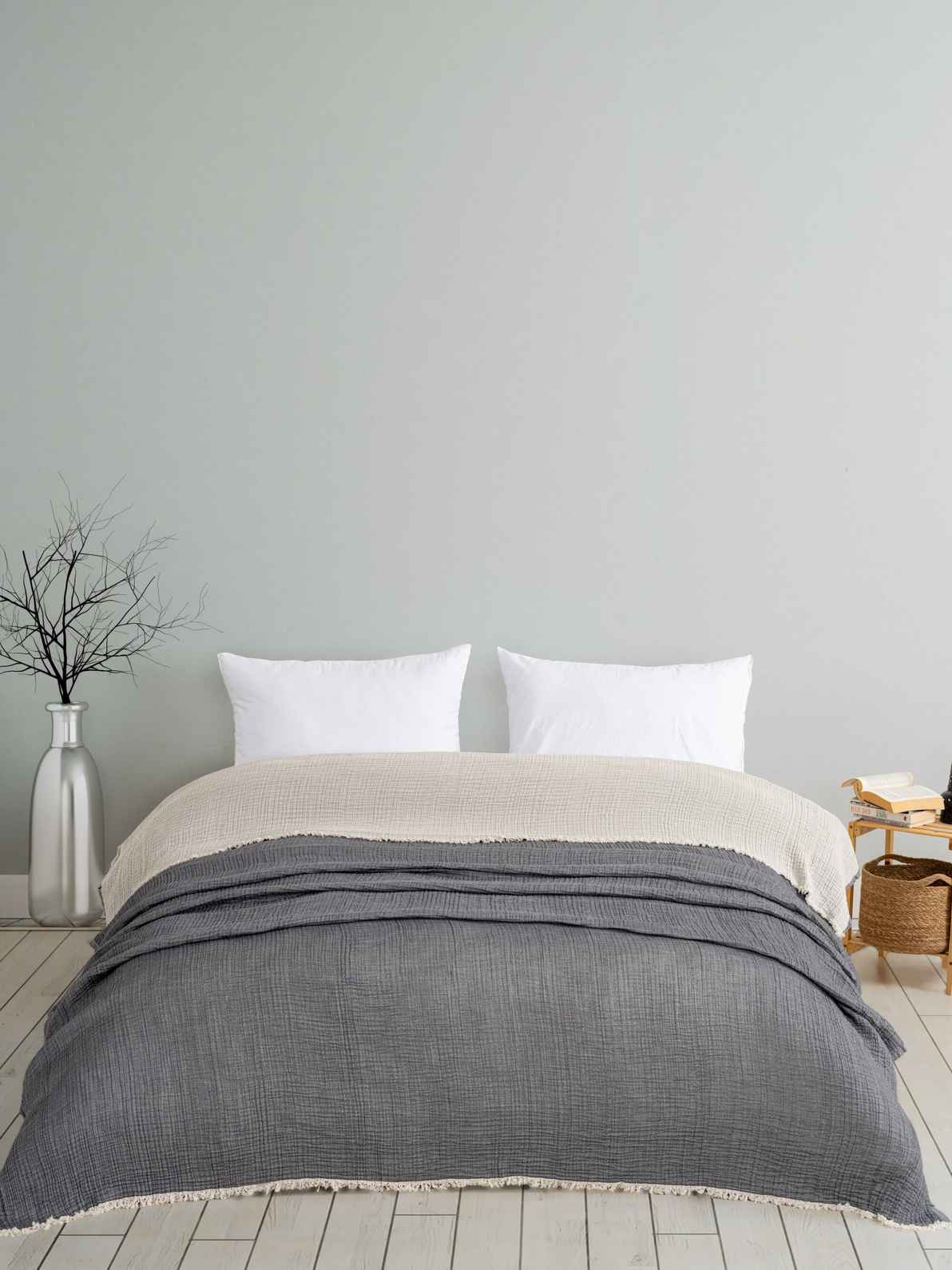 Queen bed with Premium Turkish Muslin Cotton Blanket in gray and white pillows against a light gray wall.