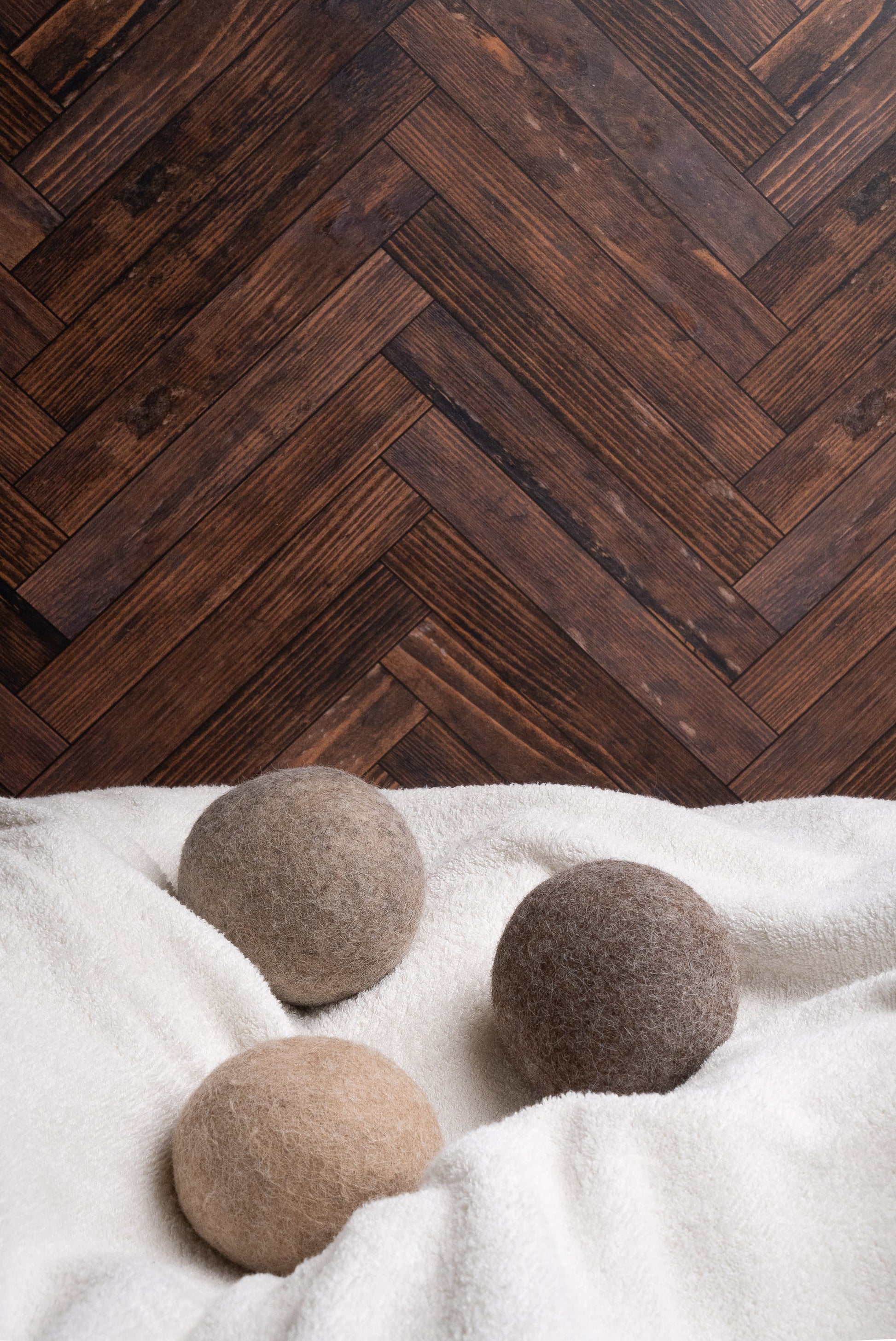 Three alpaca dryer balls on a white surface with a wooden herringbone pattern in the background