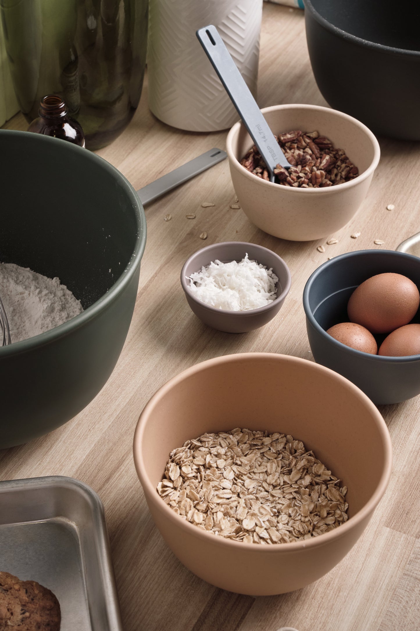 Astrik plant-based plastic nesting bowls, measuring cups and spoons filled with oats, flour, and eggs on a wooden table