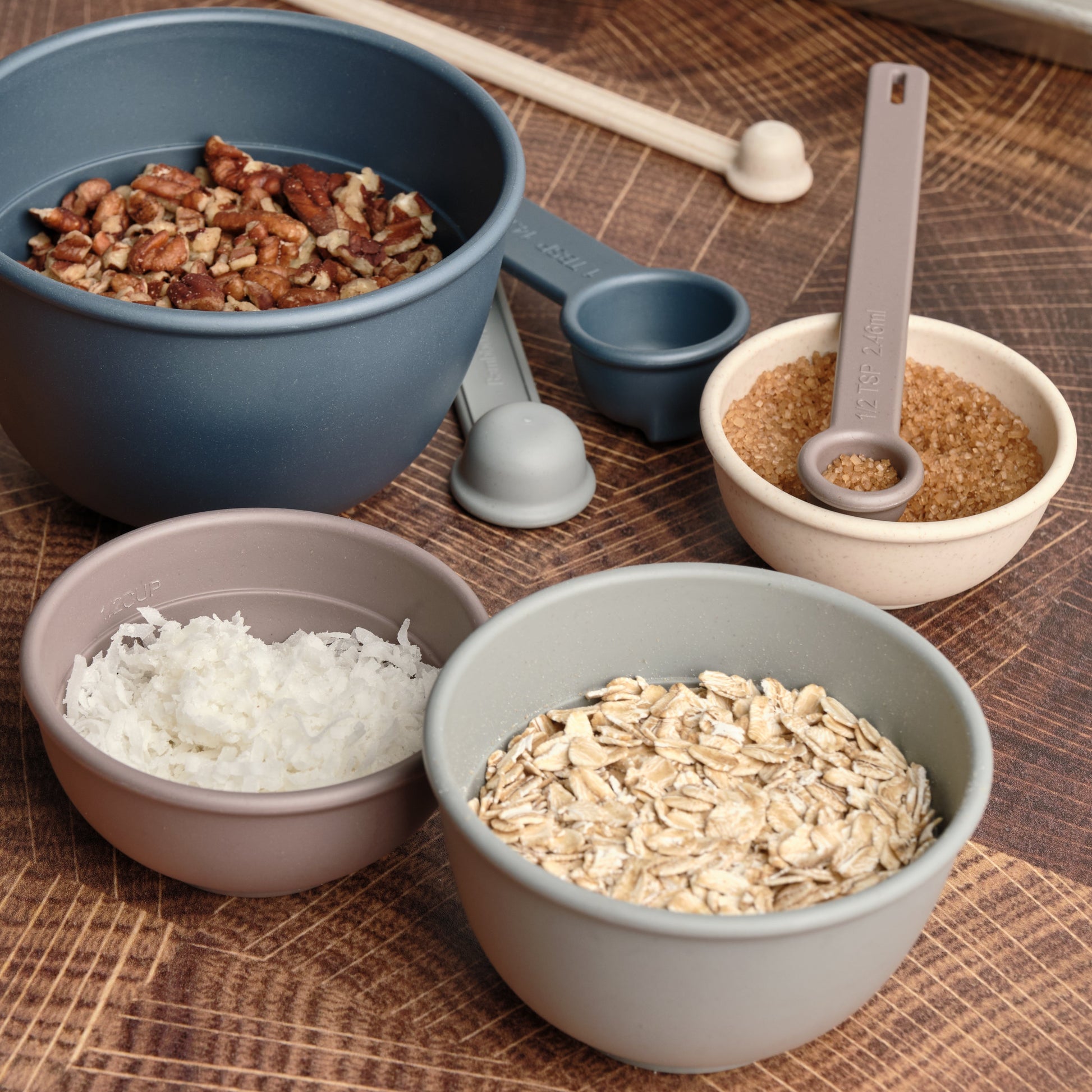 Astrik nesting bowls, measuring cups and spoons filled with various ingredients on a wooden surface