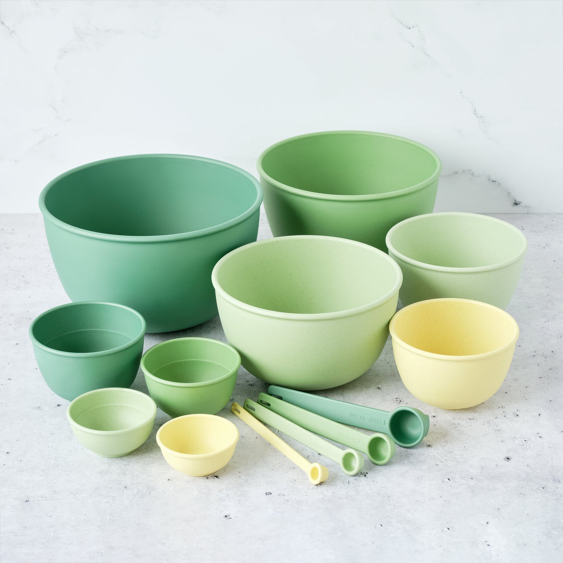 Set of Astrik mixing bowls, measuring cups and spoons in fresh guacamole (green and yellow) on a light surface