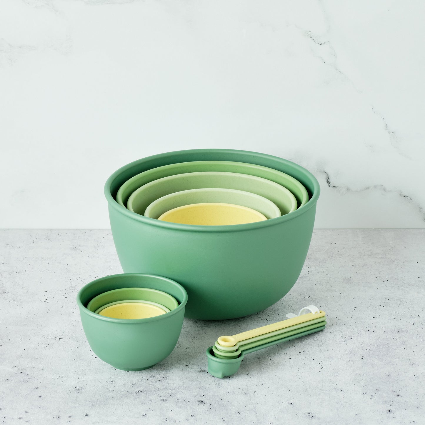 Set of Astrik nesting bowls, measuring cups and spoons in fresh guacamole (green and yellow) on a light gray surface.