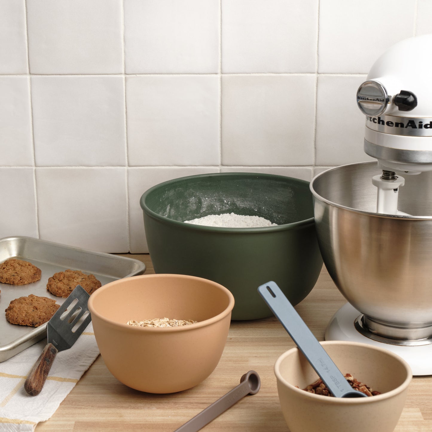 Kitchen scene with Astrik nesting bowls for baking items alongside a stand mixer and cookies on a tiled wall background.
