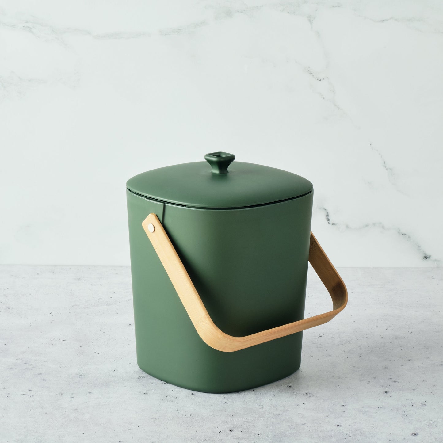 Forest-colored Astrik Compoast Bin made of 100% biodegradable plant-based plastic with a bamboo handle on a light gray background.