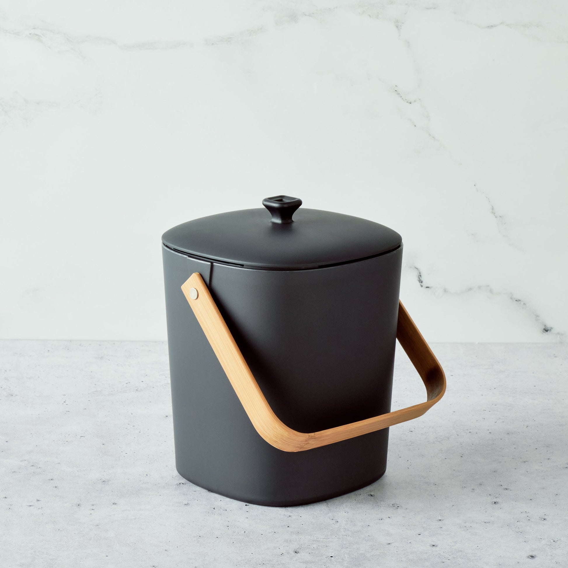 Graphite-colored Astrik Compoast Bin made of 100% biodegradable plant-based plastic with a bamboo handle on a light gray background.