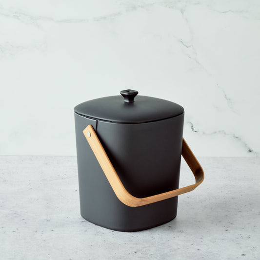 Graphite-colored Astrik Compoast Bin made of 100% biodegradable plant-based plastic with a bamboo handle on a light gray background.