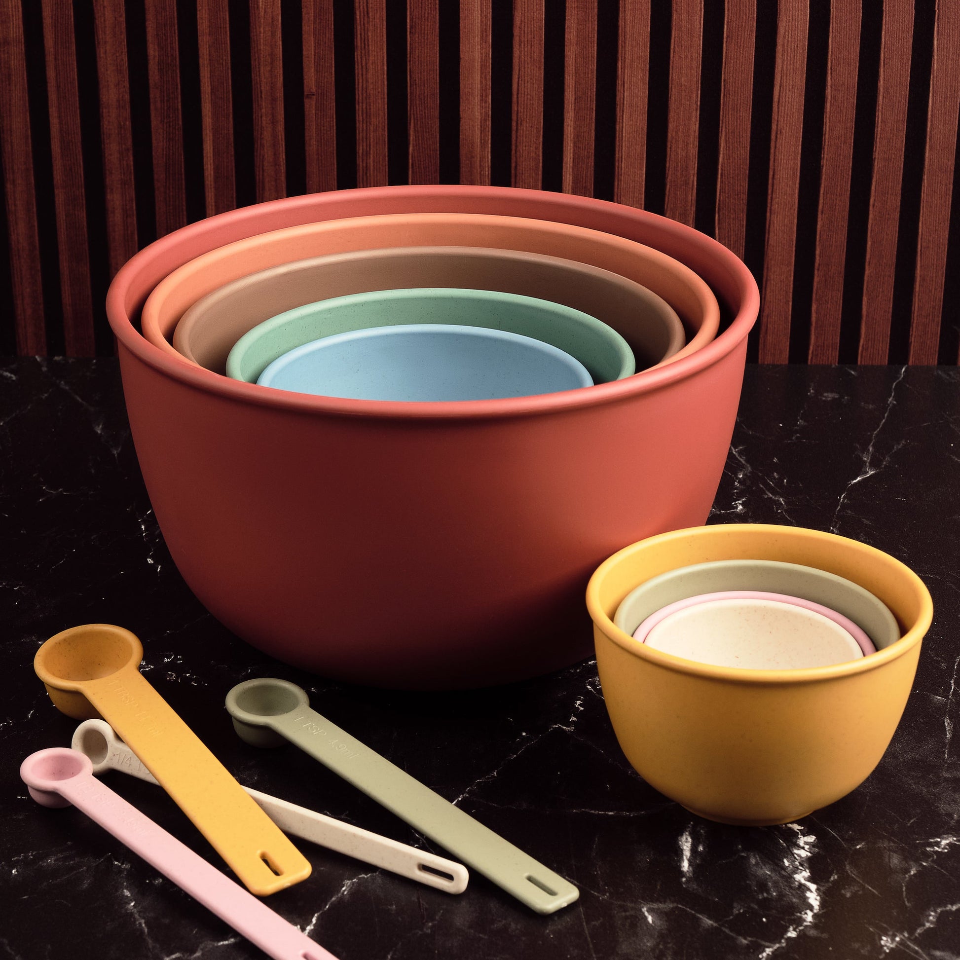 Set of Astrik nesting bowls, measuring cups and spoons in desert bloom on a dark surface with a wooden background.