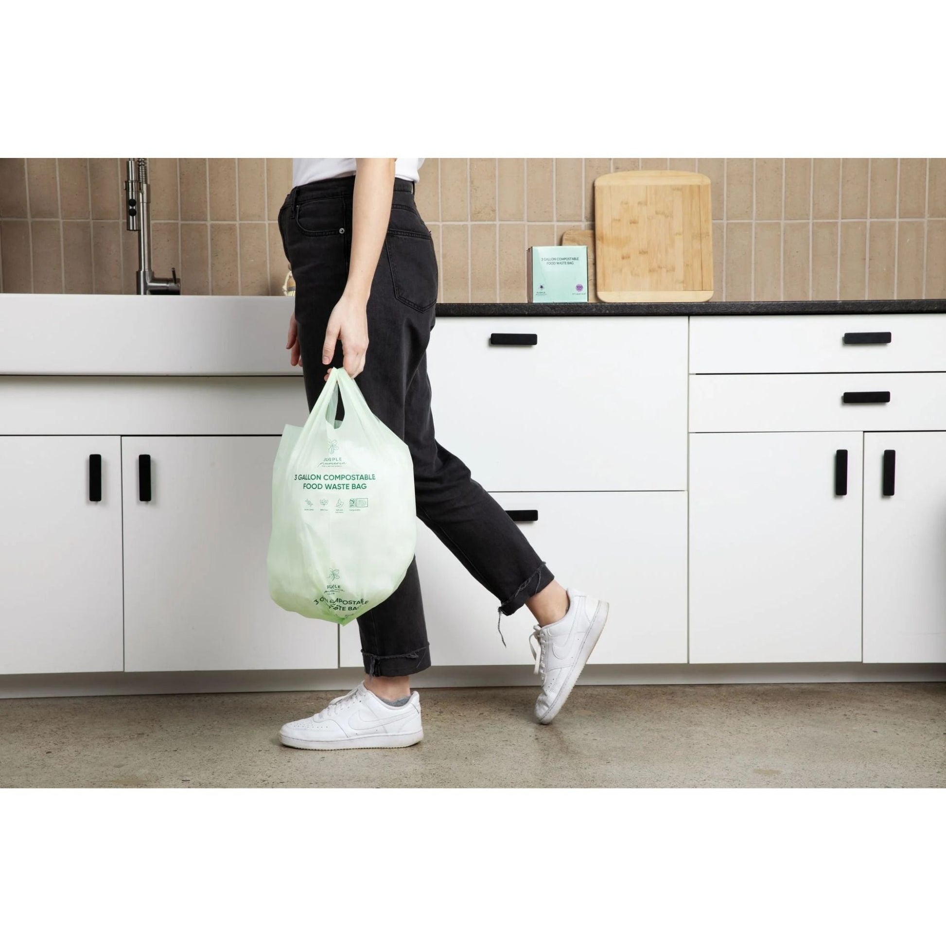 Person holding a green compostable bag in a kitchen setting