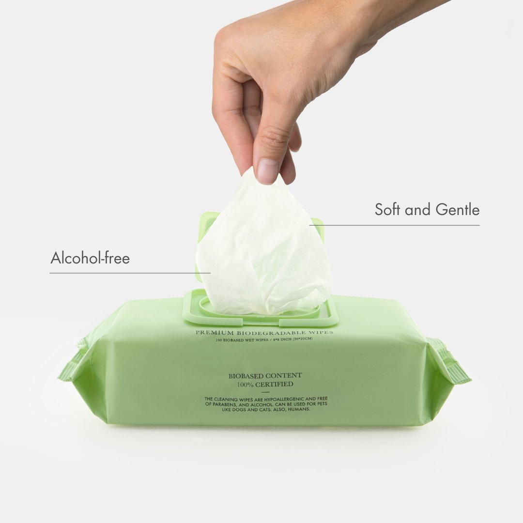 Hand pulling a Nina Woof premium biodegradable pet wet wipe from a green packet with text showcasing: alcohol-free wipe, and soft and gentle wipe on a white background