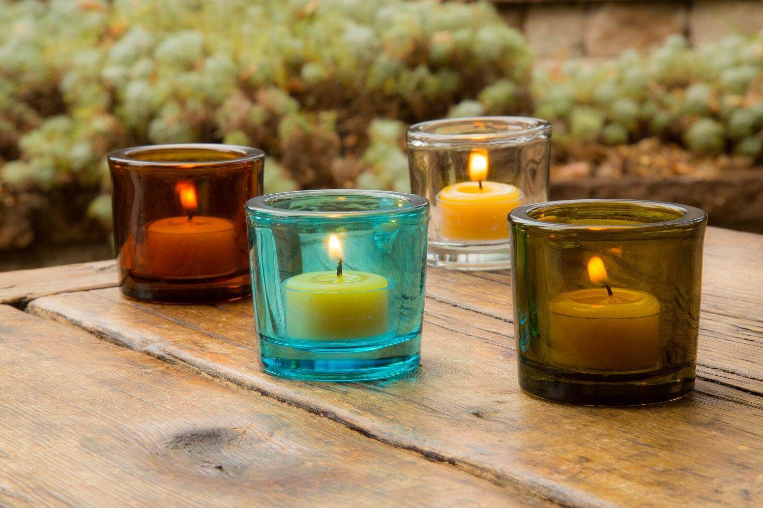 Colorful glass candle holders with lit candles on a wooden surface outdoors.