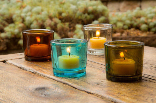 Colorful glass candle holders with lit candles on a wooden surface outdoors.
