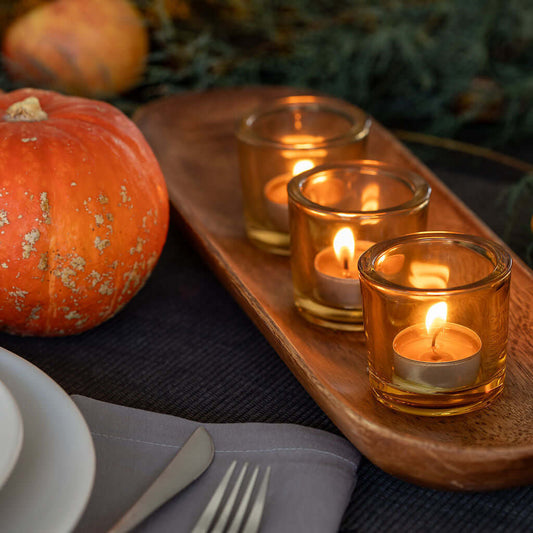 Candlelit scene with pumpkins and a wooden tray on a table, featuring Bluecorn Pure Beeswax Tea Light candles