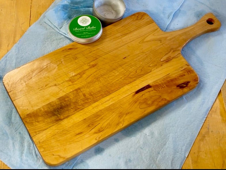 Wooden cutting board on a blue cloth with a container of board balm oil wax.