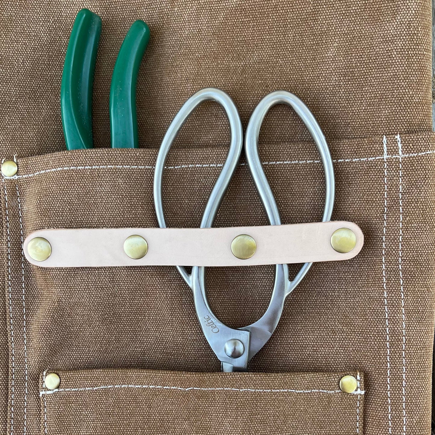 Shears and green pliers in a brown tool pouch with visible stitching