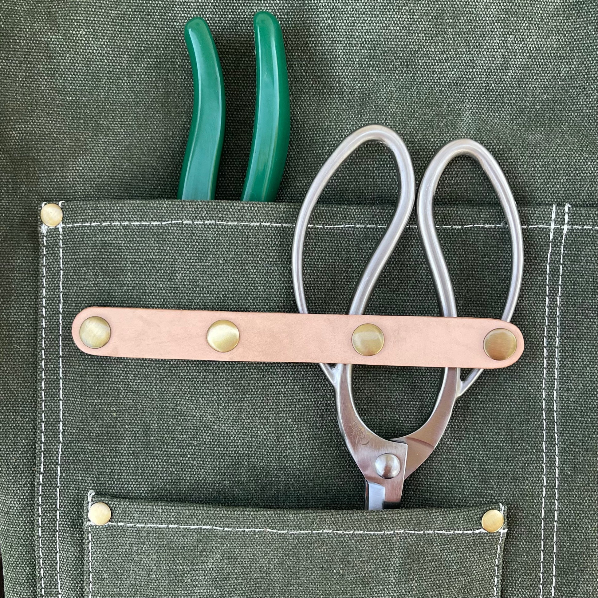 Green garden pruners with a pair of florist scissors in a garden apron pocket