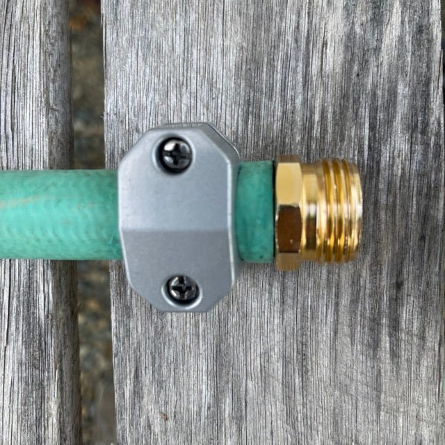 Green garden hose with a metal and brass fitting attached, on a wooden background