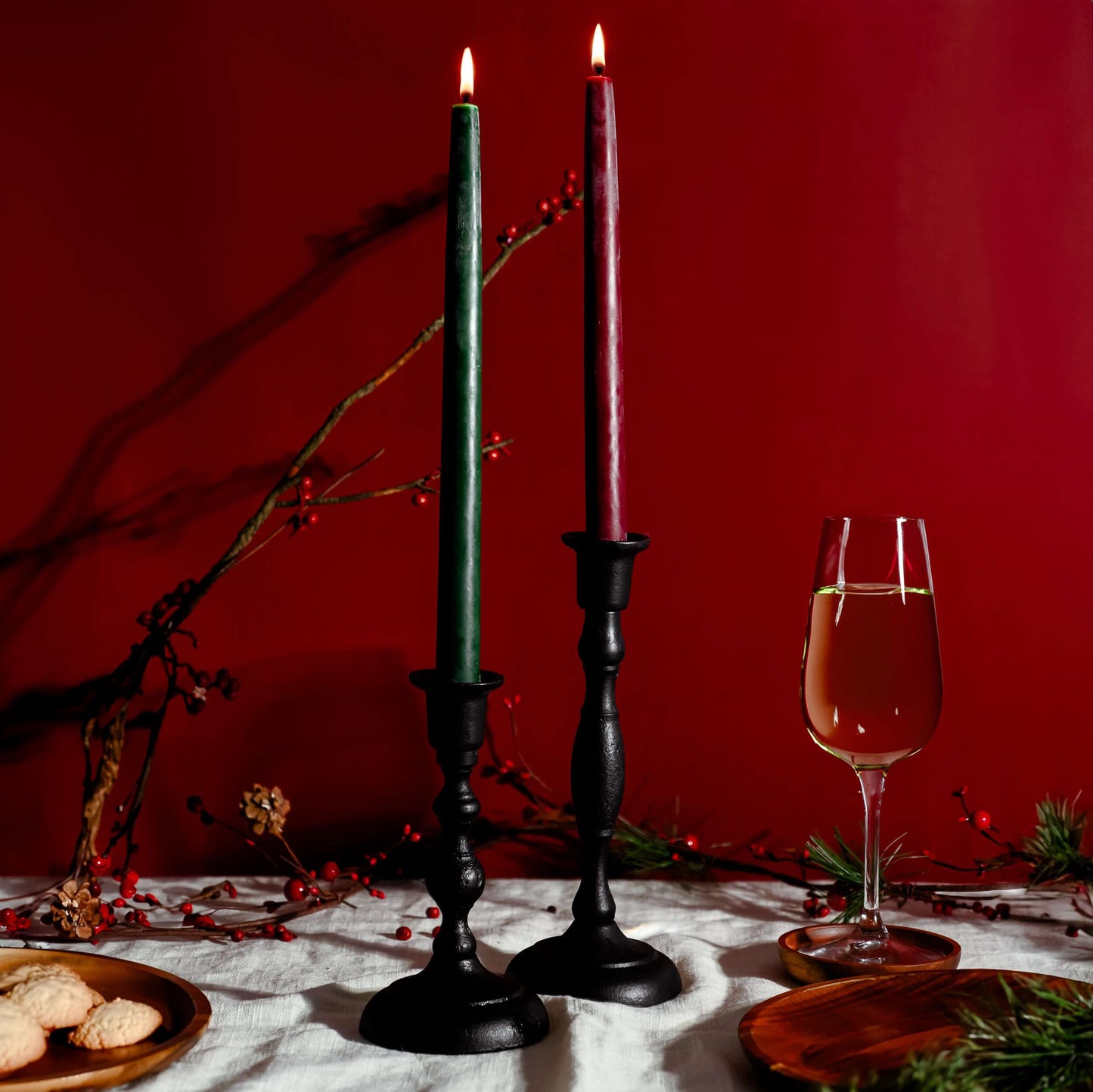 Two lit candles in black holders with a glass of wine on a red background