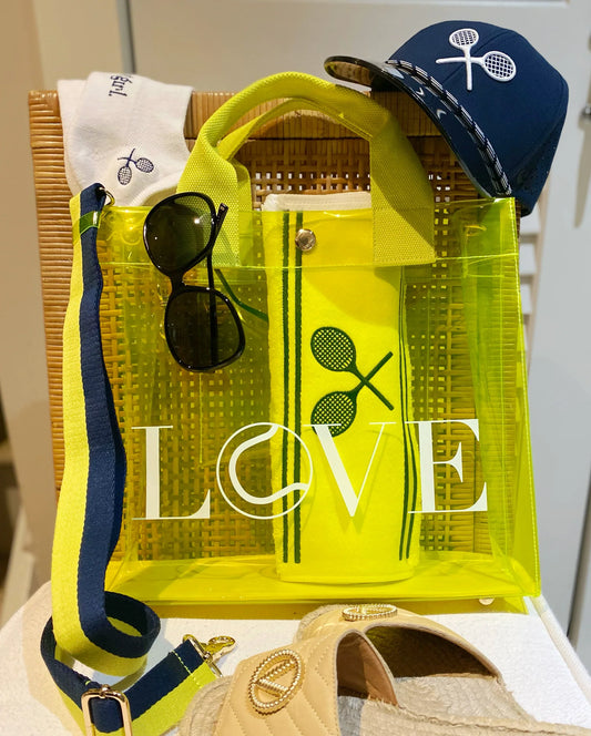 Transparent stadium-approved LOVE tote bag with minimalist design. Yellow transparent bag with 'LOVE' text, sunglasses, and a cap on a white background