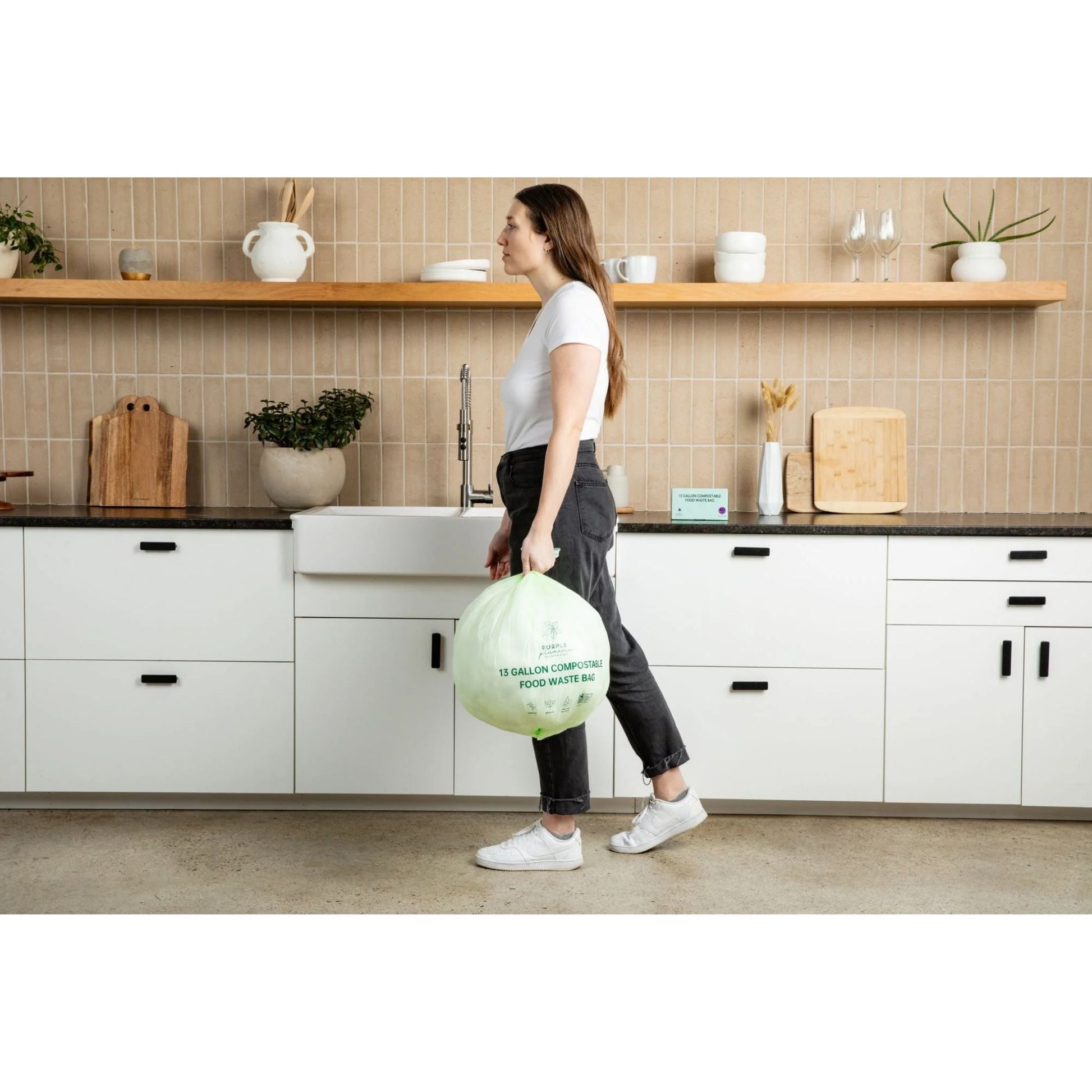 Person holding a compostable 13-gallon food waste bin in a kitchen.