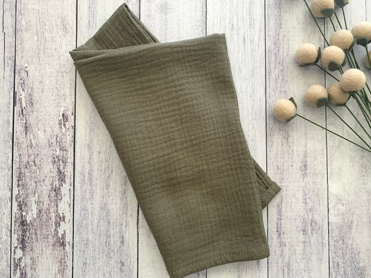 Olive Gauze 100% cotton dinner napkin from Dot and Army, arranged on a wooden surface