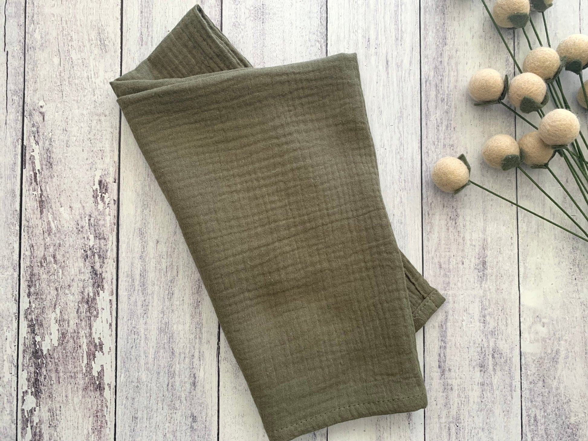 Olive Gauze 100% cotton dinner napkin from Dot and Army, arranged on a wooden surface