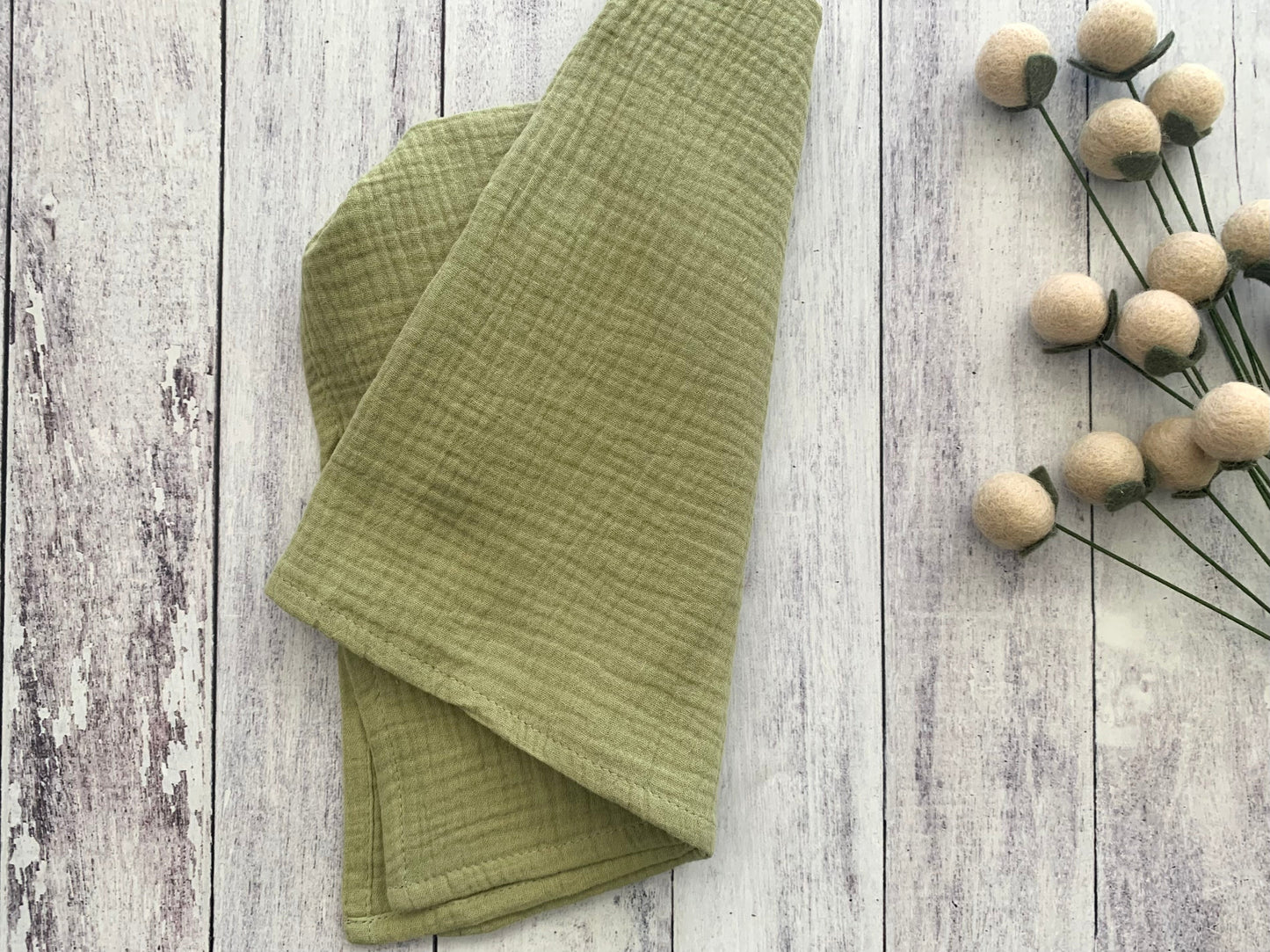 Sage 100% cotton dinner napkin from Dot and Army, arranged on a wooden surface