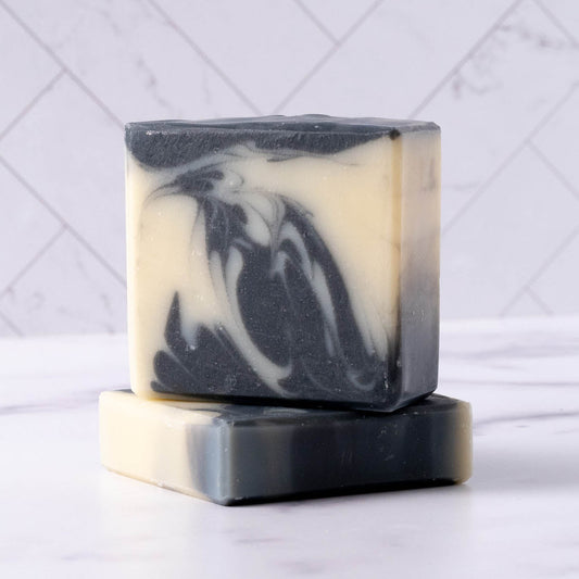 Two bars of detoxifying charcoal black and white soap stacked on a white background