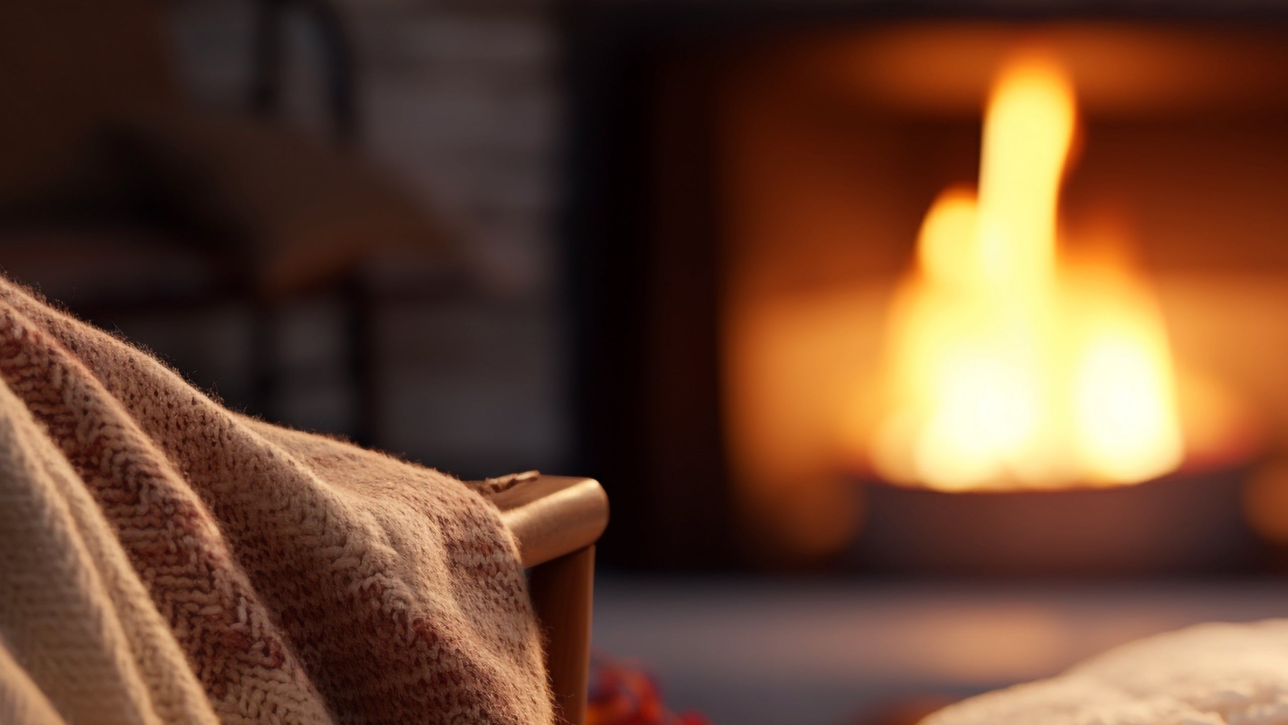 Cozy scene with a blanket draped over a chair in front of a fireplace.