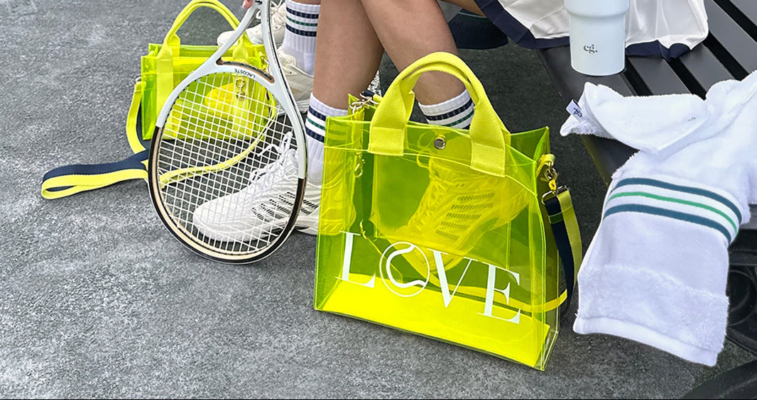 Eco-friendly transparent LOVE tote made from durable biodegradable material. Person holding a transparent yellow 'LOVE' bag with tennis racket and shoes in the background