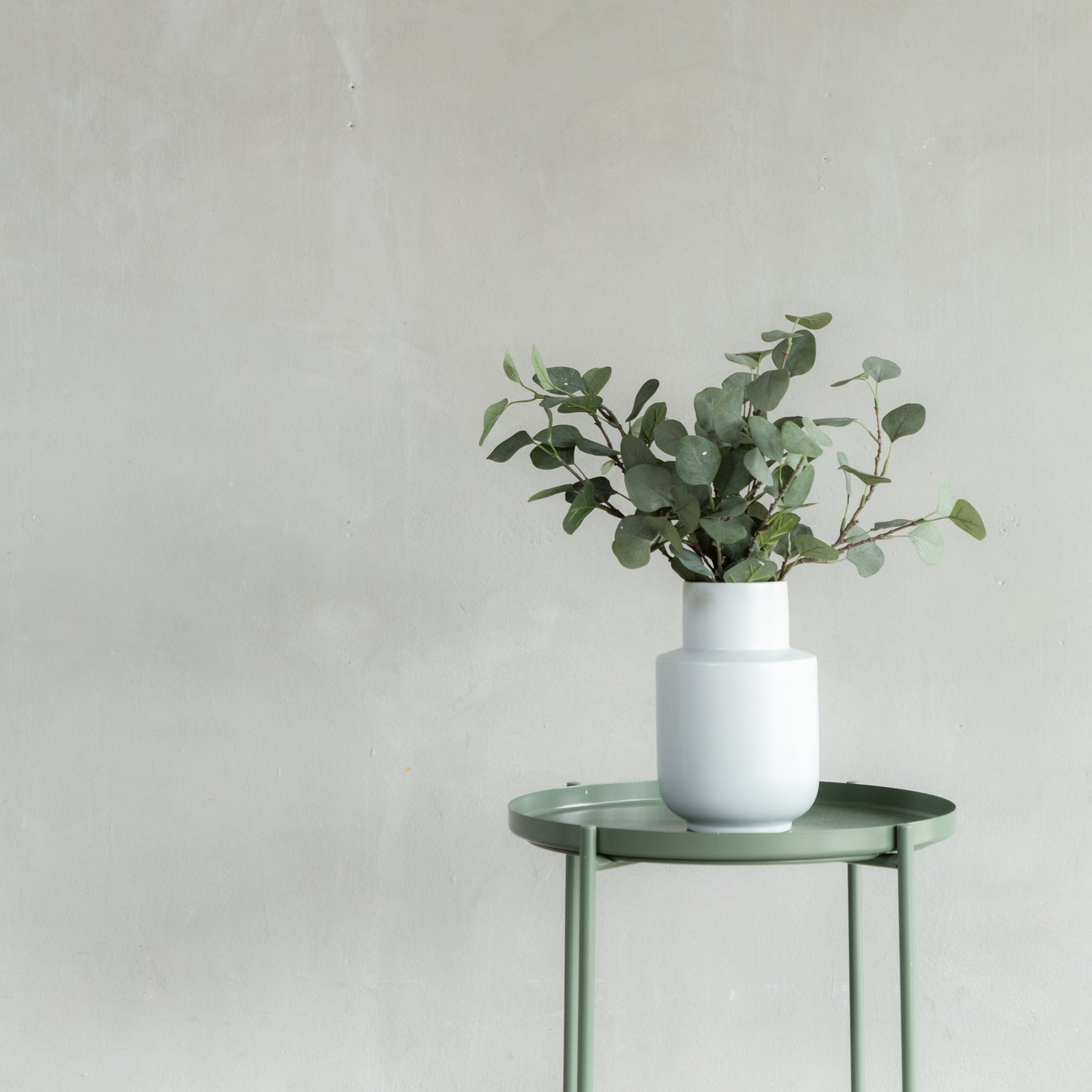 Eucalyptus in white vase on green table.