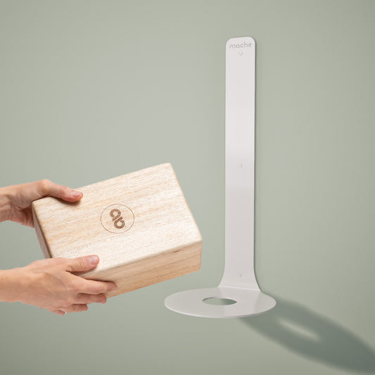 Wooden yoga block in hands by a floating yoga block shelf mounted on the wall on a gray background