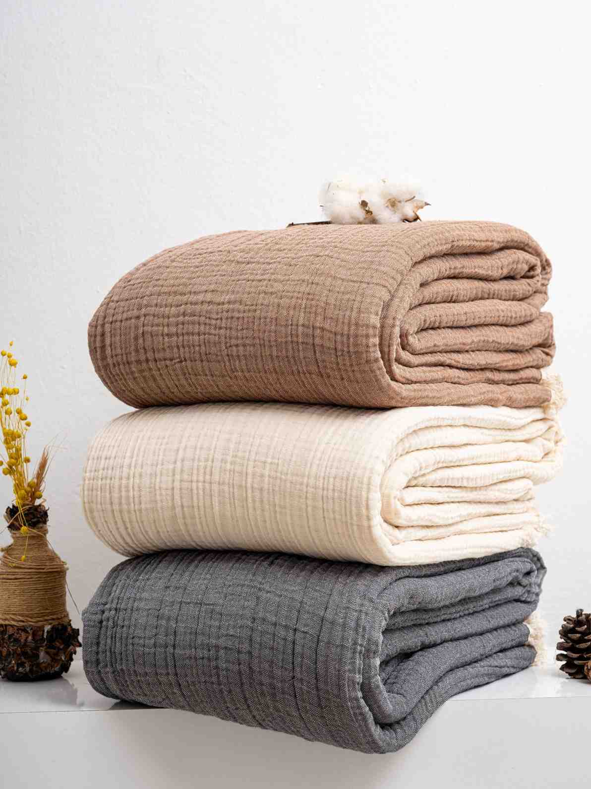 Stack of folded Premium Turkish Muslin Cotton Blankets in brown, white, and gray on a white surface with decorative elements.