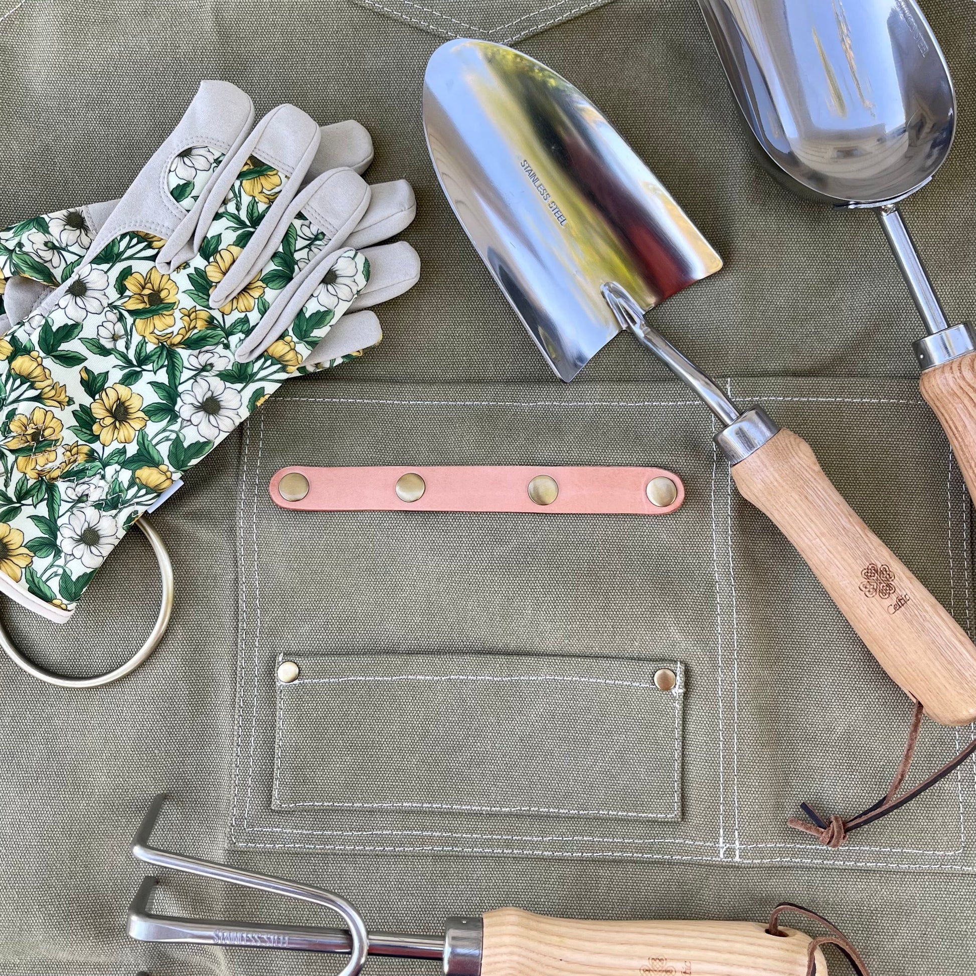 Gardening tools including a trowel, pruner, and gloves on a green apron.