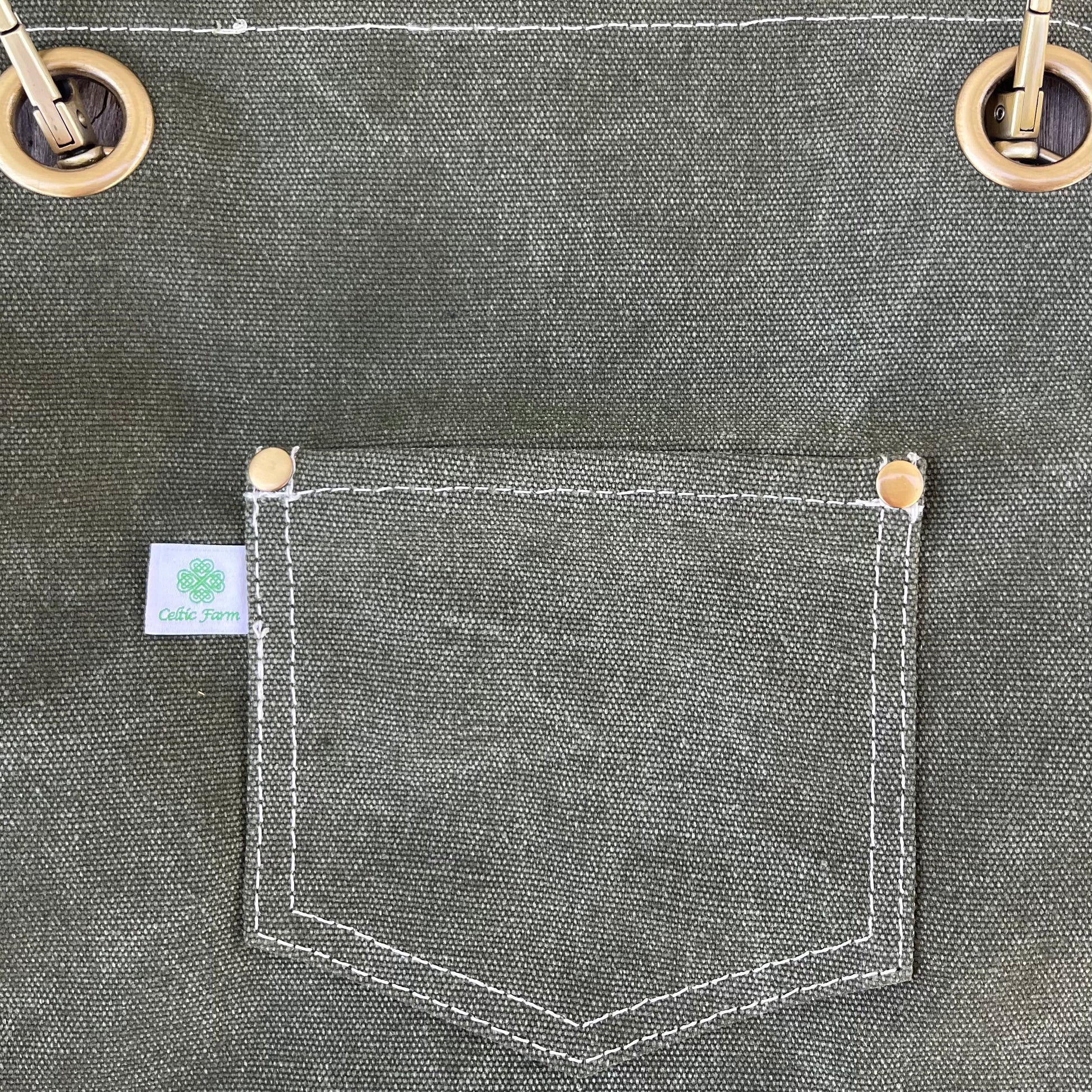 Close-up of a waxed canvas pocket on a garden apron with metal grommets, featuring a brand label for Celtic Farm.