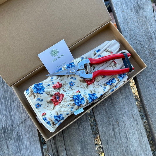 Floral-patterned gardening gloves and stainless steel snippers in a cardboard box on a wooden surface