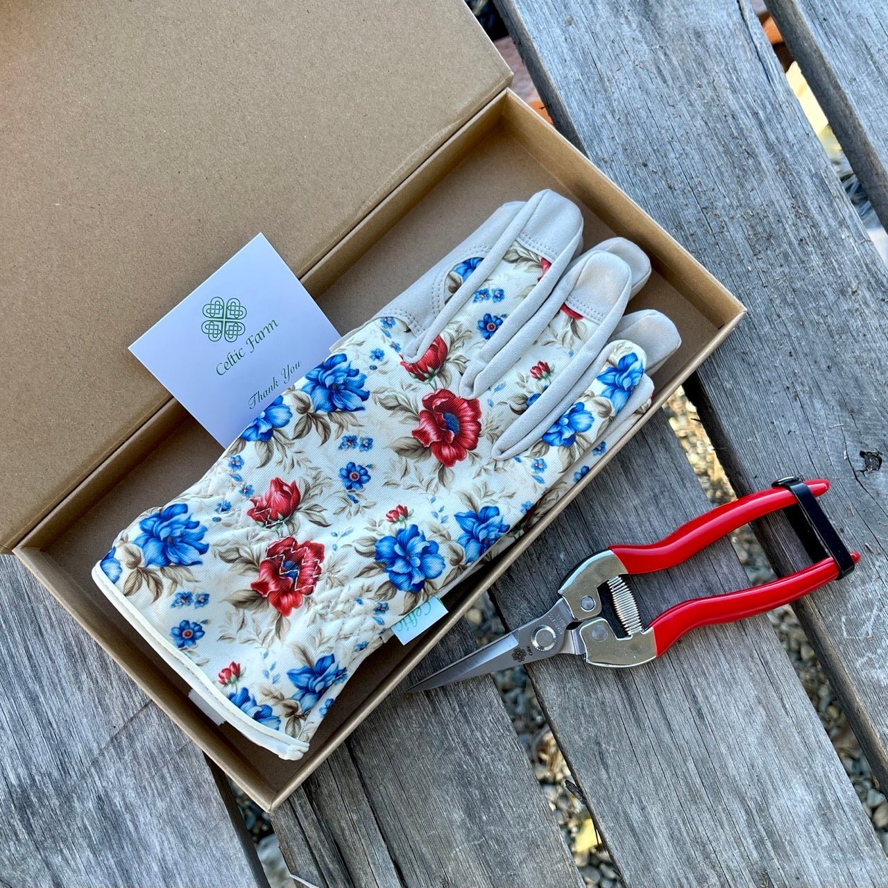 Floral-patterned gardening gloves in a box with a pair of pruning snippers on a wooden surface.