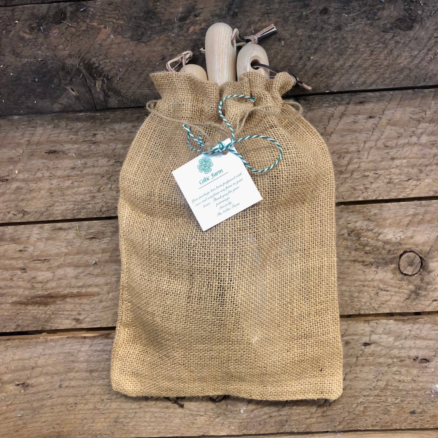 Burlap bag with wooden garden tool set items and a tag on a wooden surface