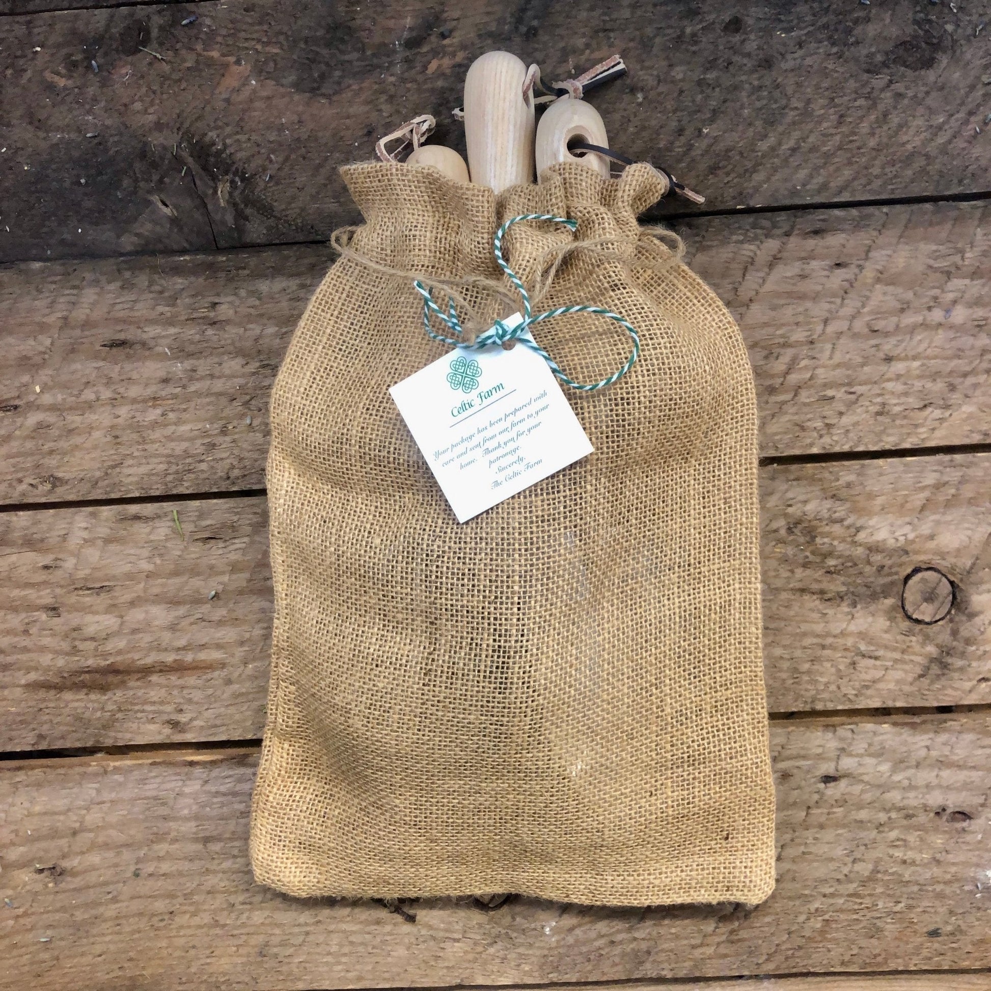 Burlap bag with wooden garden tool set items and a tag on a wooden surface