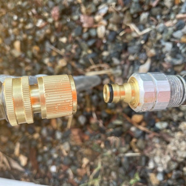 Close-up of two brass garden hose nozzles against a gravel background