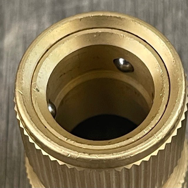 Close-up of a brass hose fitting with a threaded interior on a metallic background