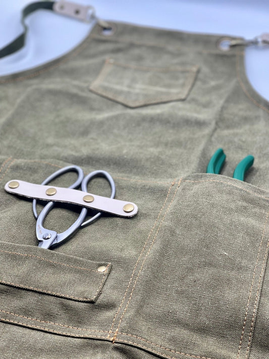 Green garden apron with a pair of pruning sheers in one of the pockets on a gray background