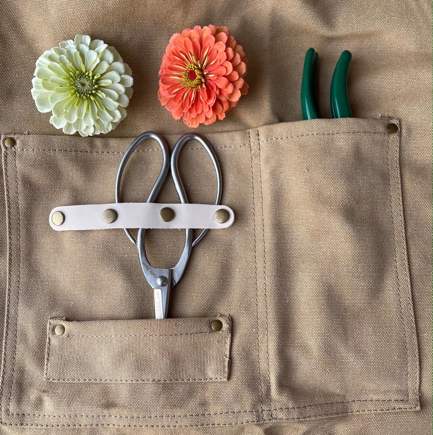 Florist sheers, garden pruners, and flowers in the pockets of a waxed canvas garden apron.
