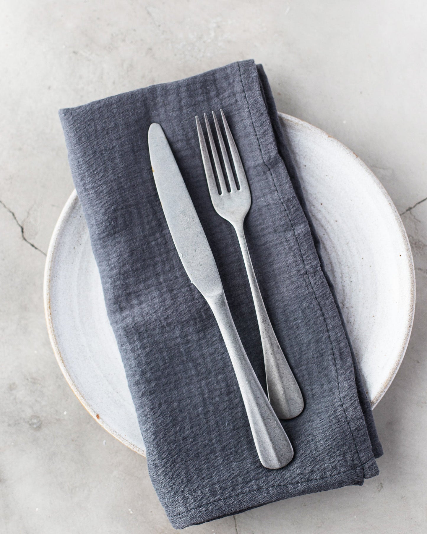 Gray 100% cotton dinner napkin from Dot and Army, arranged with silverware on a white plate