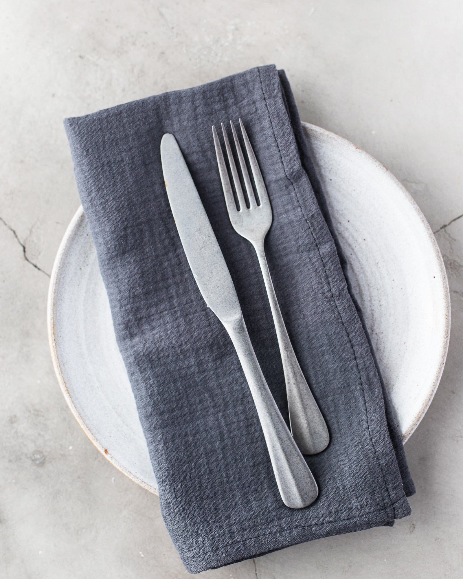 Gray 100% cotton dinner napkin from Dot and Army, arranged with silverware on a white plate