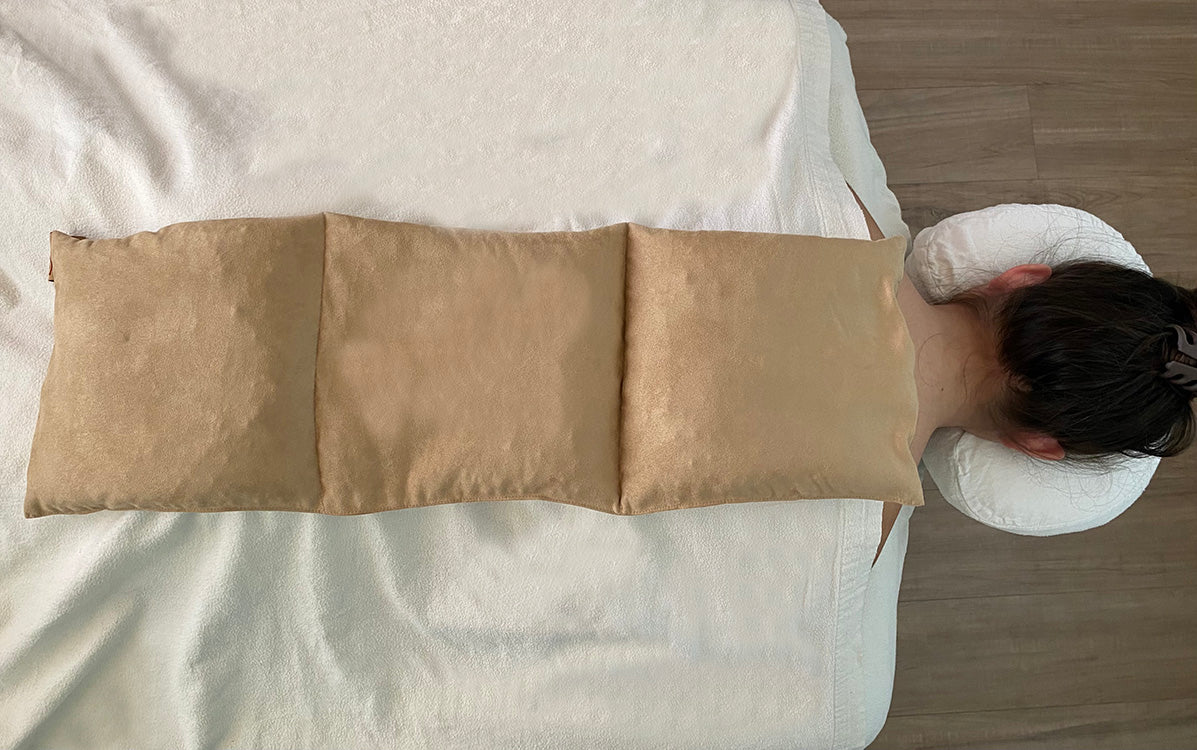 Person lying on a massage table with a Hot Cherry Triple Square Pillow Maraschino Ultra Suede Heating Pad across the length of their back