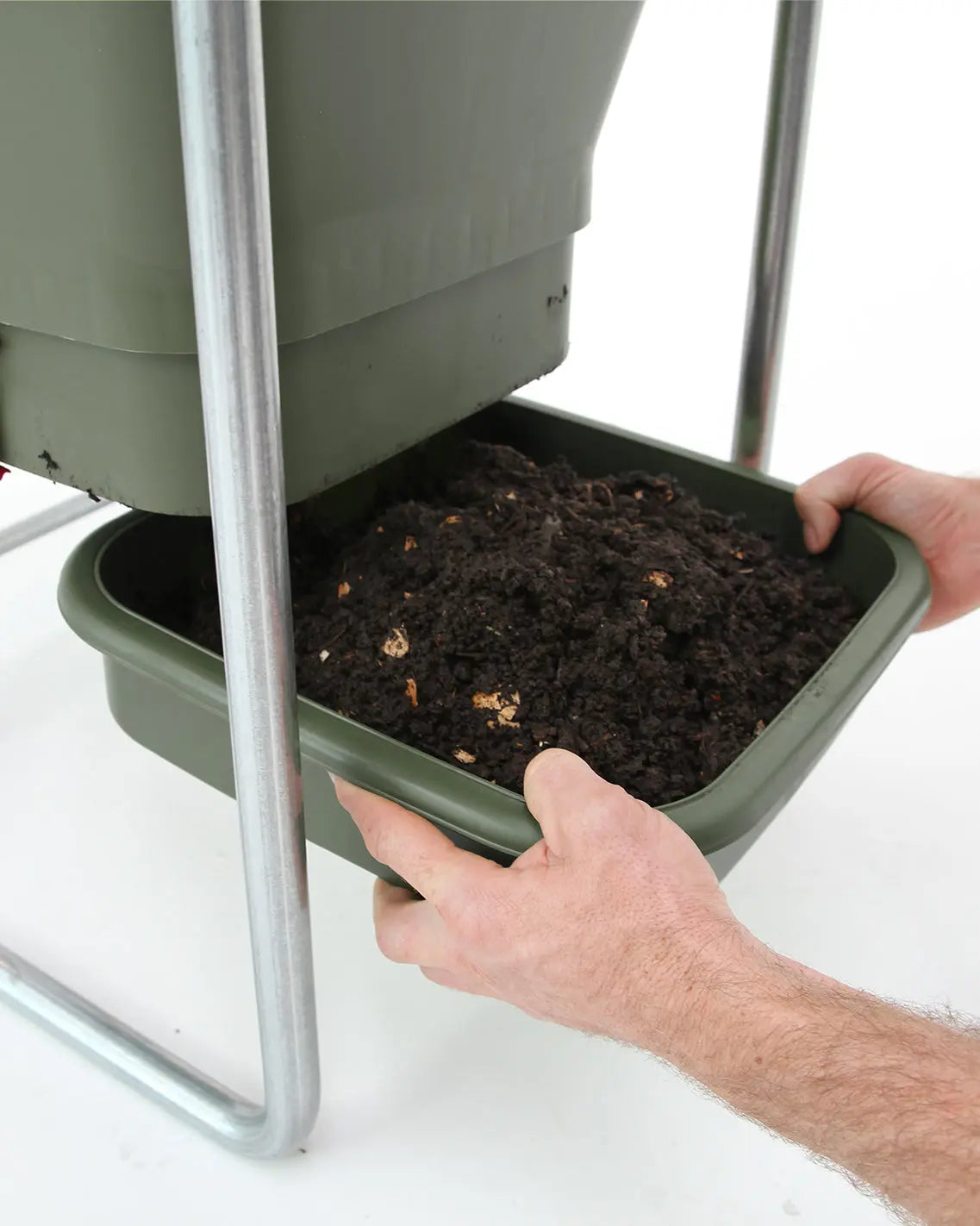 Person removing the green worm casting tray from the Hungry Bin Compost Bin with worm castings on a white background