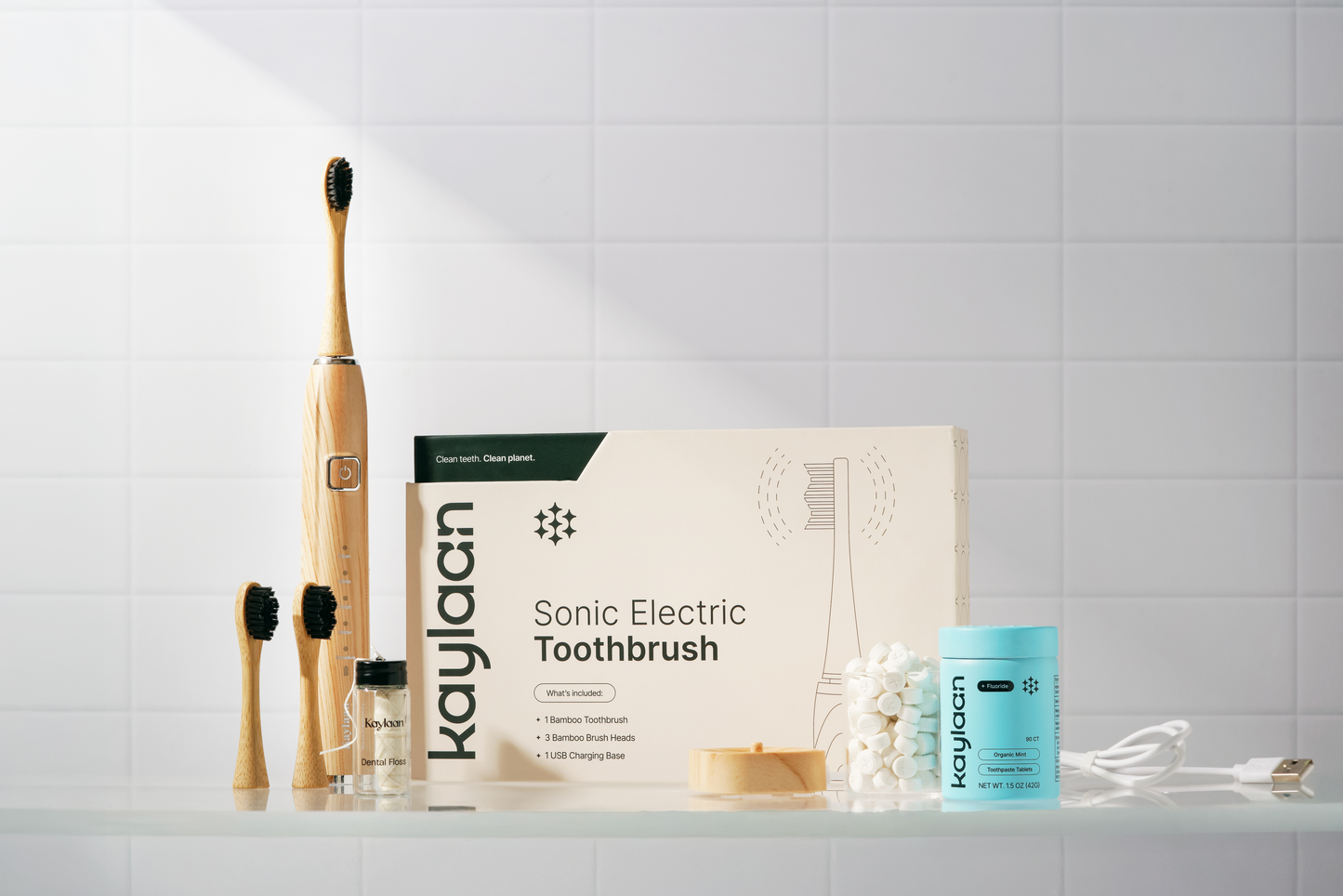 Kaylann sonic electric toothbrush set, including an electric bamboo toothbrush and replacements heads on a tiled bathroom counter.