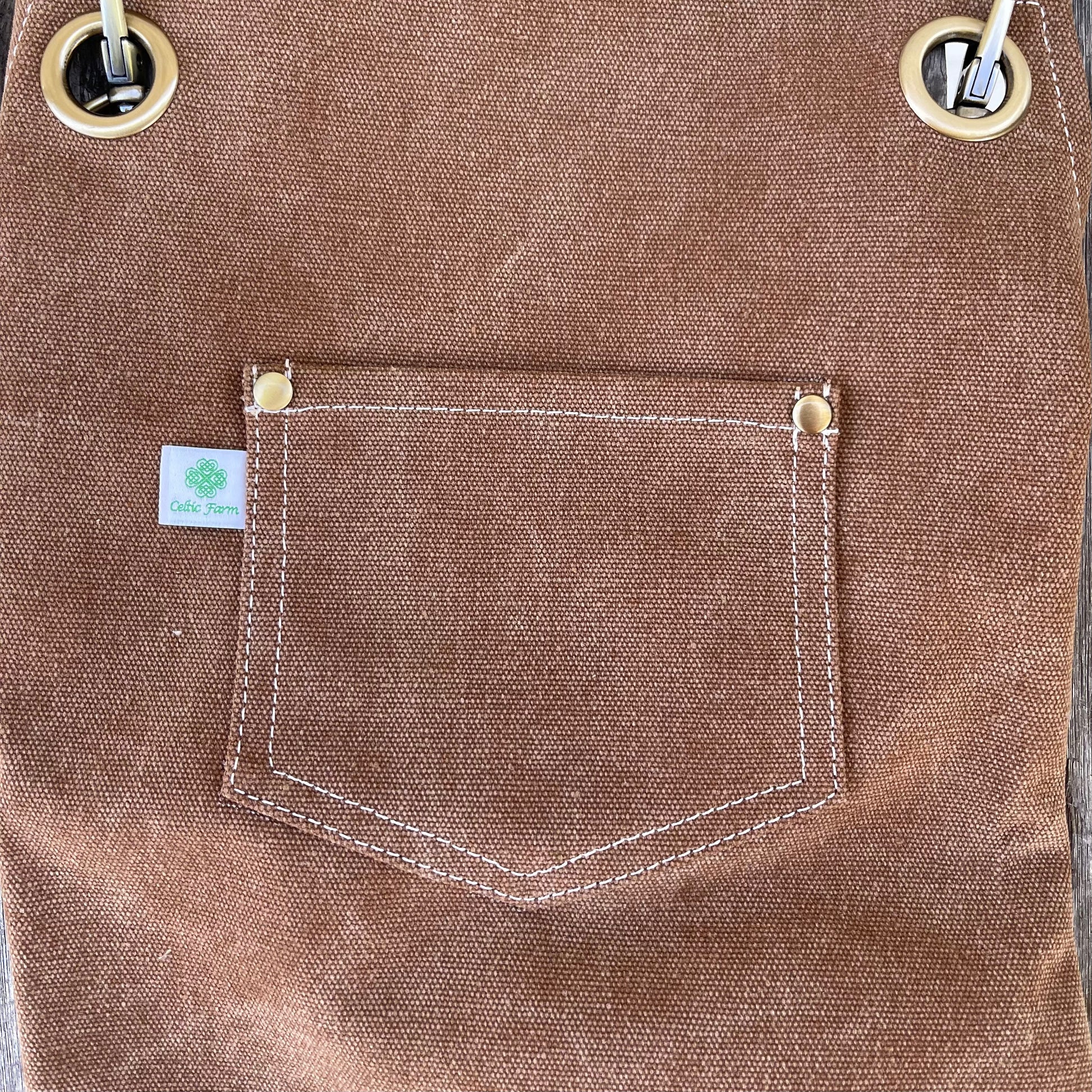 Mocha leather apron with a pocket and button closures, featuring a brand label.