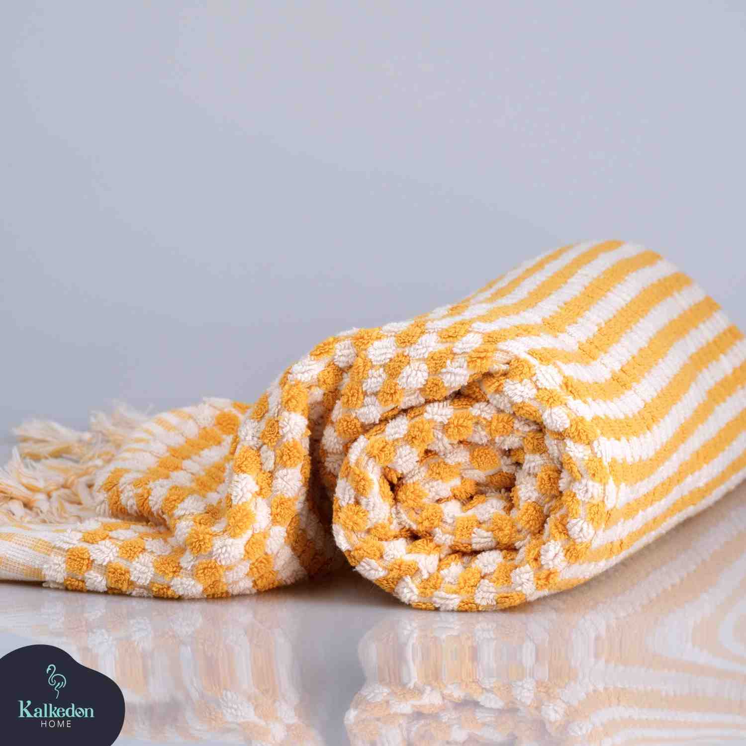 Mustard and white striped Premium 100% Organic Turkish Cotton Jacquard Bath Towel rolled up on a reflective surface with a light gray background